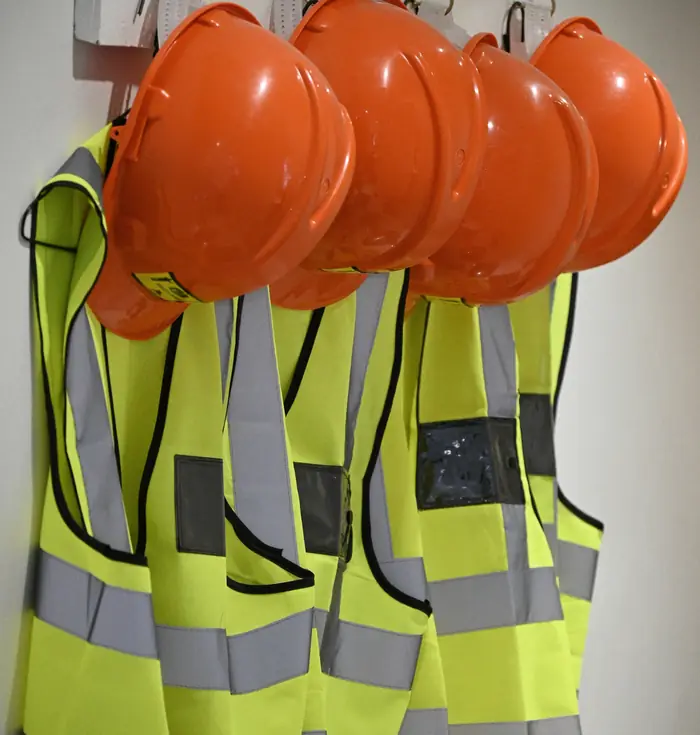 Orange hard hats hanging on hooks above hi-vis vests in a site cabin