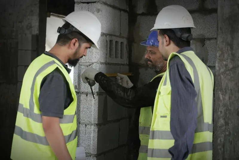 Three operatives in hard hats and hi-vis check measurements on a blockwork wall