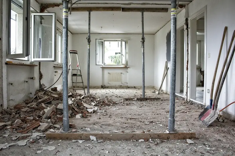 A room stripped back to bare walls with steel props supporting the ceiling and rubble swept into piles
