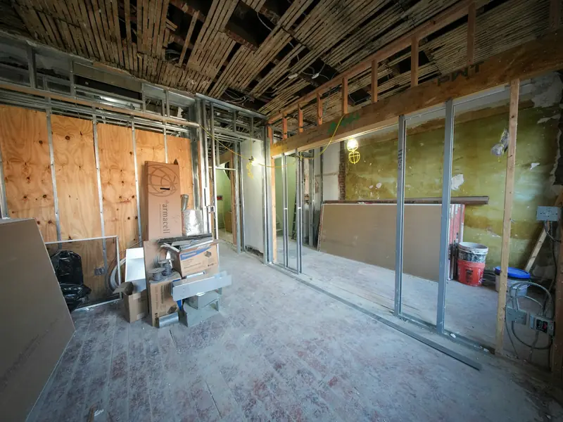 An office floor mid strip-out: ceiling grid gone, studwork partitions exposed, materials sorted into stacks